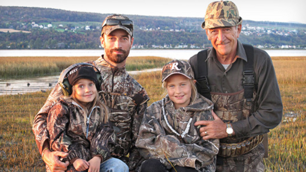 Deux hommes et deux enfants habillées en chasse dans un champs. 